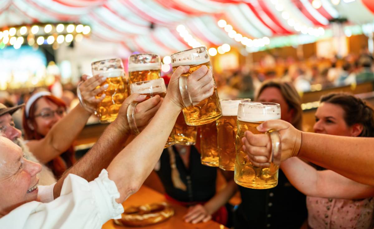 na zdjęciu uchwycony moment w którym uczestnicy Oktoberfest stukają się kuflami, świętując i bawiąc się
