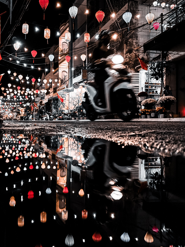 Nocna ulica w Hoi An w Wietnamie z kolorowymi lampionami i przejeżdżającym skuterem odbijającym się w mokrej nawierzchni