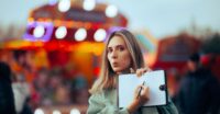 Woman Showing her Empty Bucket List in Fun Fair Festival. Travel girl thinking what to do and write in a vacation journal