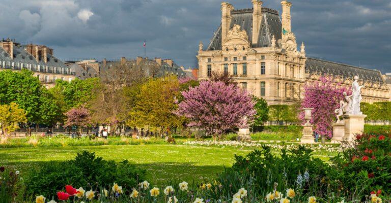 fragment Luwru w Paryżu. Budynek widoczny w tle to Pavillon de Flore – jedno ze skrzydeł kompleksu Luwru, który znajduje się przy Ogrodach Tuileries (Jardin des Tuileries), które widzisz na pierwszym planie z pięknie kwitnącymi drzewami i kwiatami. Shutterstock