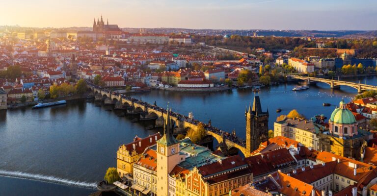 Panoramiczne zdjęcie Pragi z lotu ptaka o zachodzie słońca, z Mostem Karola przecinającym Wełtawę, gotyckimi wieżami, barokową zabudową i kompleksem Hradczan w tle shutterstock