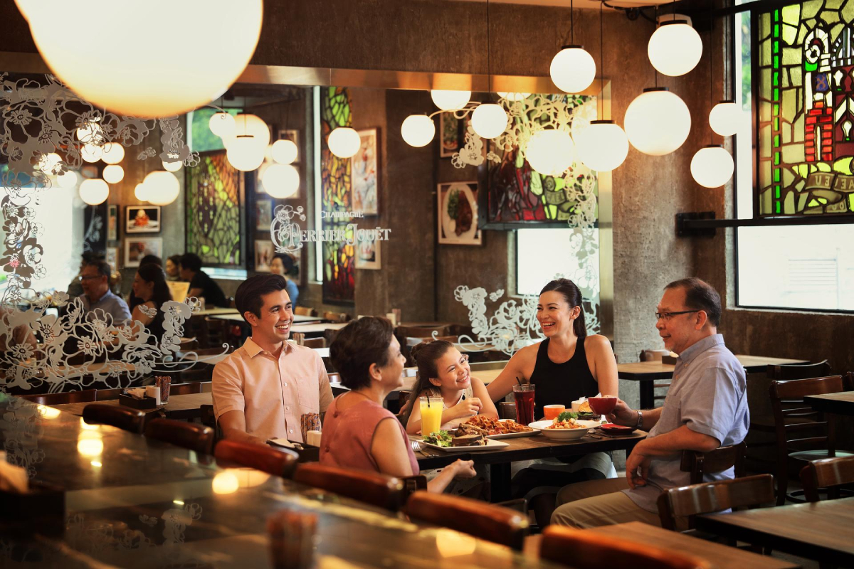 Singapur, Stół jadalny Ludzie Ciepła atmosfera, Nassim Hill Bakery Bistro Bar
Grupa ludzi siedzi przy stole w restauracji. Widocznych jest pięć osób, w tym młoda dziewczyna. Otaczają ich potrawy i napoje. Restauracja ma ciepłą i przyjazną atmosferę, z oświetleniem kulistym i witrażowymi oknami. W tle widoczni są inni goście.
