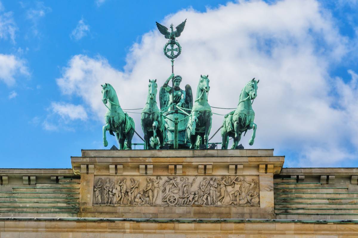 Rzeźba kwadrygi na szczycie Bramy Brandenburskiej w Berlinie – przedstawienie bogini zwycięstwa powożącej czterokonnym rydwanem, na tle błękitnego nieba z chmurami.
