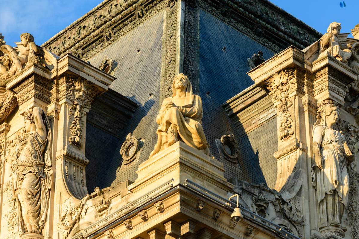 Zbliżenie na detale architektoniczne i rzeźby jednej z fasad Luwru, oświetlone ciepłym światłem.