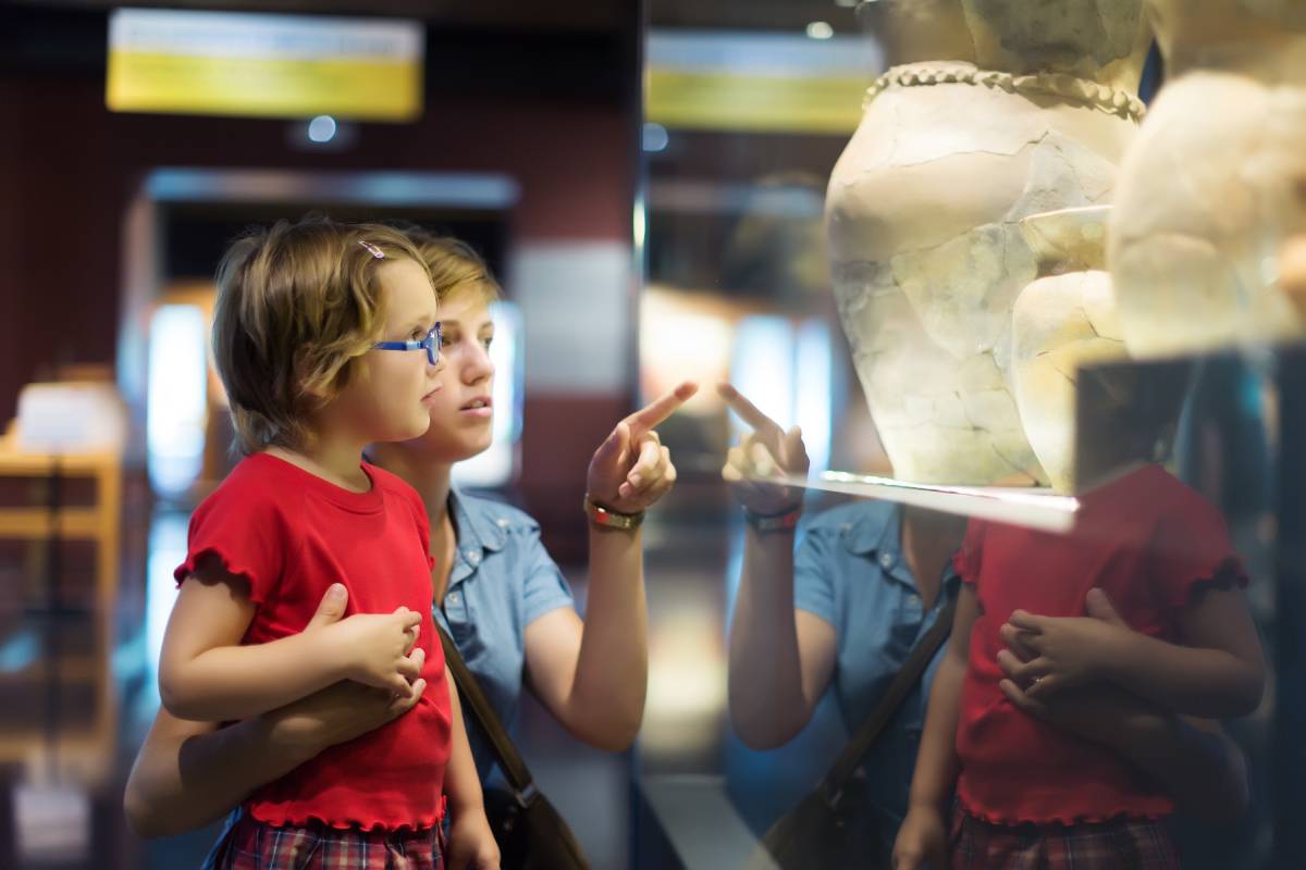 Dziecko i opiekun oglądają starożytne naczynie za szybą w muzeum, wskazując na szczegóły eksponatu.