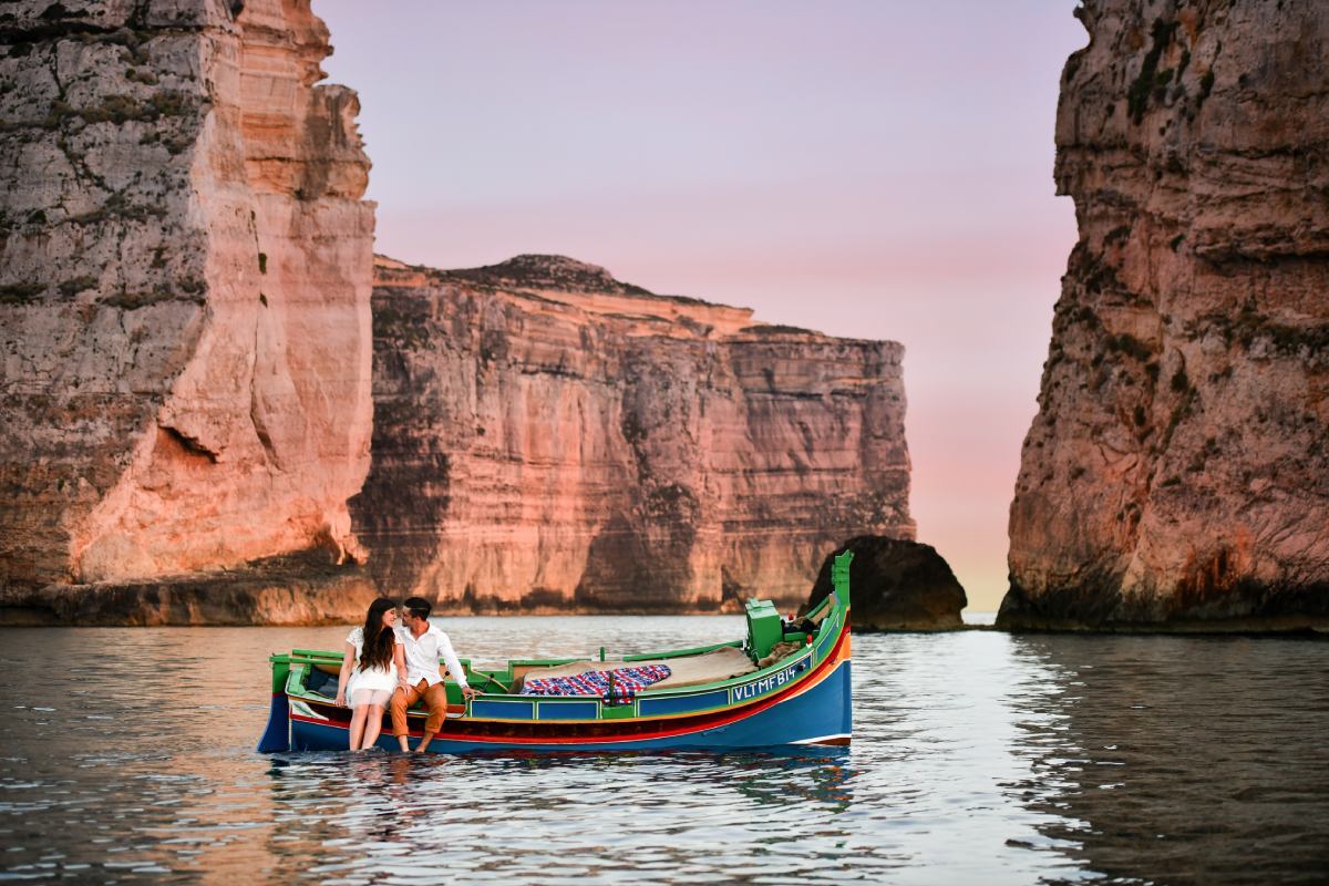 Para podczas romantycznego rejsu tradycyjną maltańską łodzią luzzu w Dwejra Bay na Gozo, Malta, o zachodzie słońca.