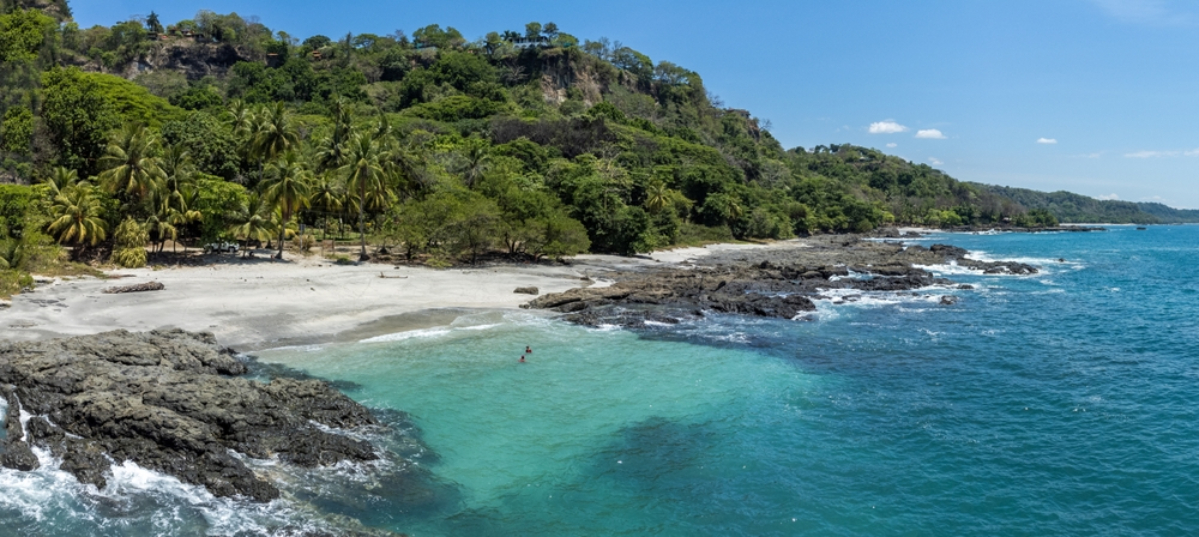 Widok z drona na tropikalną plażę Montezuma na półwyspie Nicoya w Kostaryce – turkusowa woda Oceanu Spokojnego, skaliste wybrzeże i bujna roślinność w jednym z najpiękniejszych regionów Ameryki Środkowej. Blue Zone