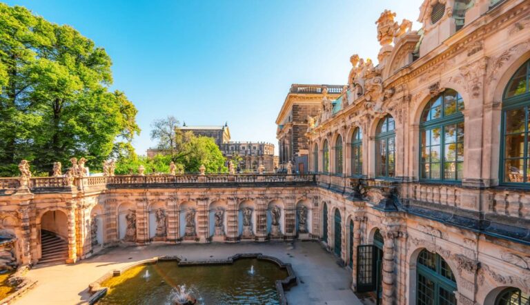 Dziedziniec pałacu Zwinger w Dreźnie z fontanną, zdobioną barokową fasadą i rzeźbami, w otoczeniu zielonych drzew i zabytkowych budynków w słoneczny dzie