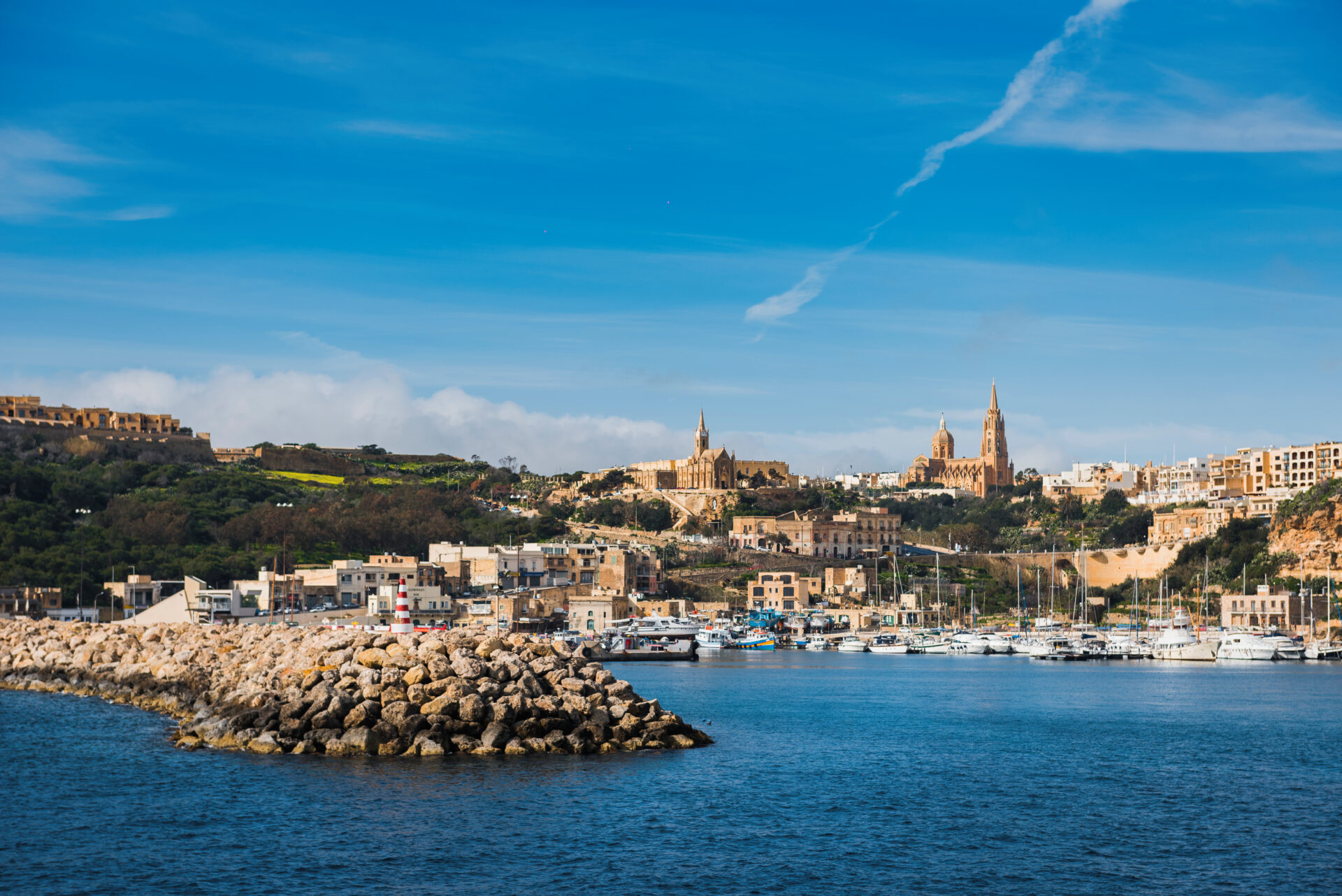 Widok na port Mgarr na wyspie Gozo na Malcie z mariną, zabudowaniami i charakterystycznym kościołem na wzgórzu.