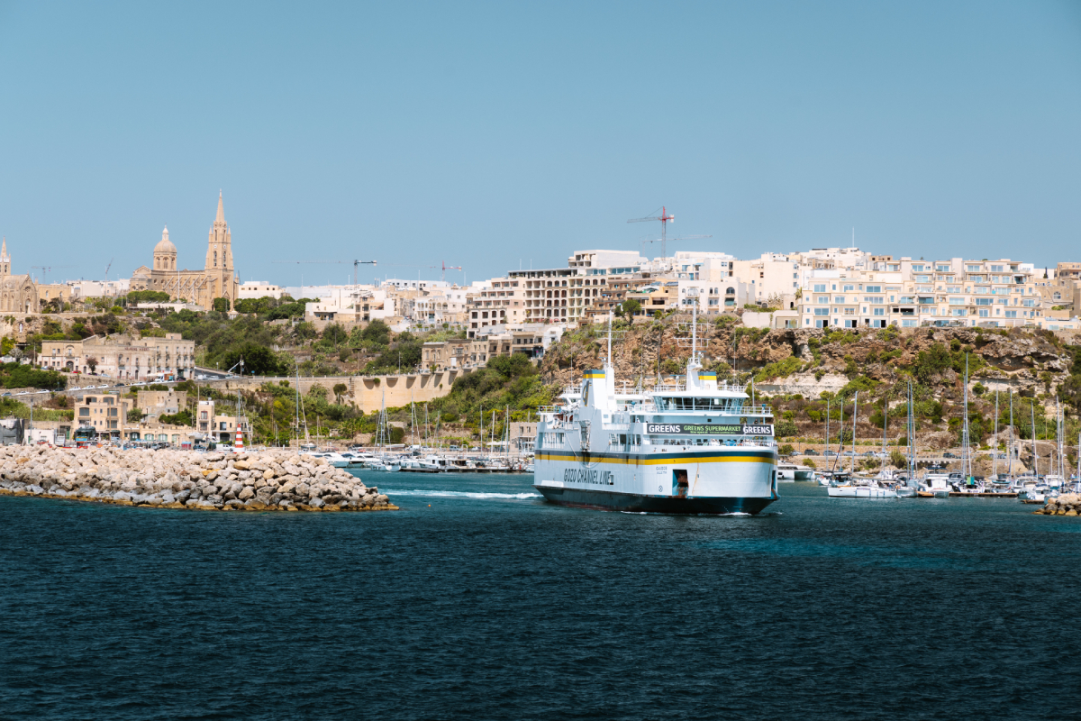 Prom Gozo Channel Lines wpływający do portu Mgarr na wyspie Gozo, Malta, z widokiem na miasteczko i kościół na wzgórzu.