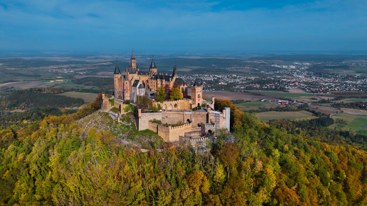 Zamek Hohenzollern w Niemczech widziany z lotu ptaka, otoczony jesiennym lasem i wzgórzami.