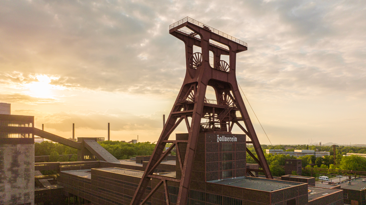 Zeche Zollverein w Essen, Niemcy, historyczny kompleks przemysłowy UNESCO. Widok na charakterystyczny, stalowy szyb kopalniany w zachodzącym słońcu, symbol Zagłębia Ruhry i dziedzictwa industrialnego Nadrenii Północnej-Westfalii. [c] Tourismus NRW e.V.